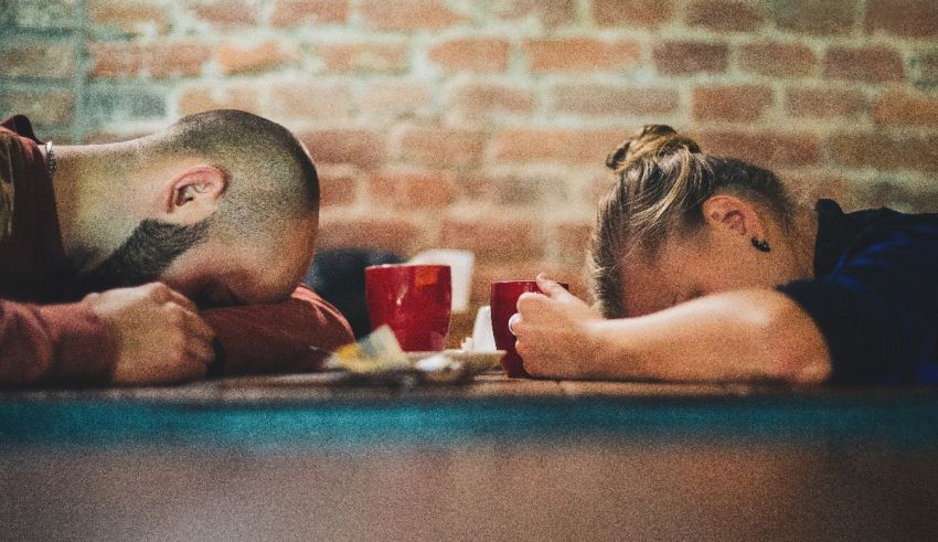 Two people sleeping at a table with coffee mugs.