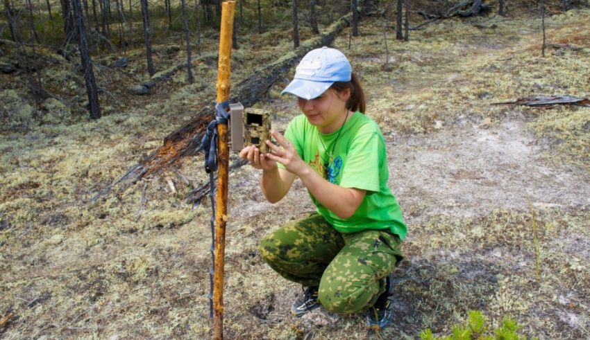 A woman in a green shirt is kneeling down in a forest.