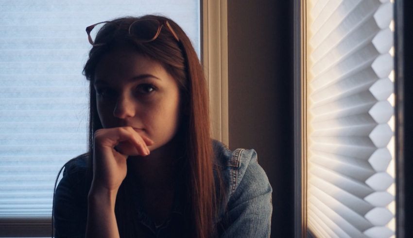 A girl sitting in front of a window with blinds.
