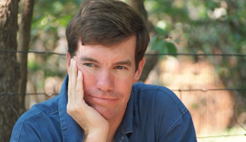 A man in a blue shirt leaning against a fence.