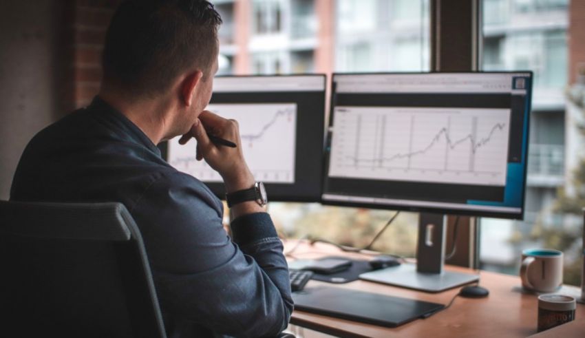 A man sitting at a desk with two monitors in front of him.