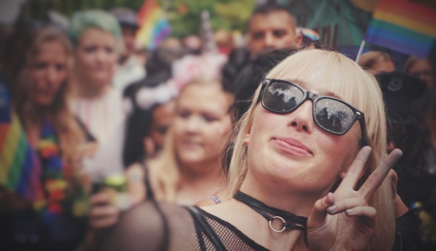 A woman wearing sunglasses and holding a peace sign in front of a crowd of people.