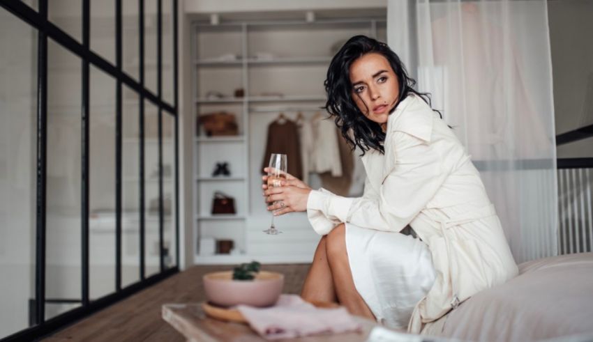 A woman is sitting on a bed holding a glass of wine.