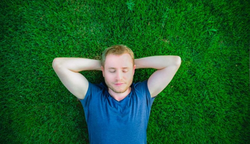 A man laying on the grass with his hands on his head.