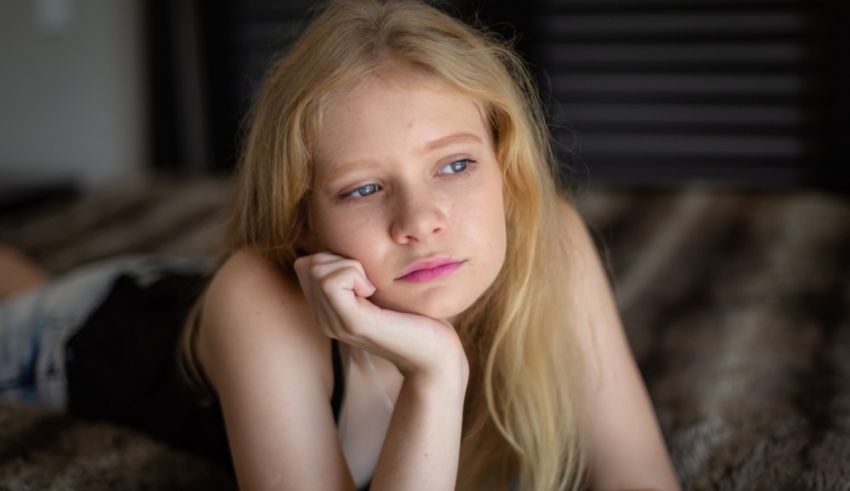 A young girl laying on a bed with her hand on her chin.