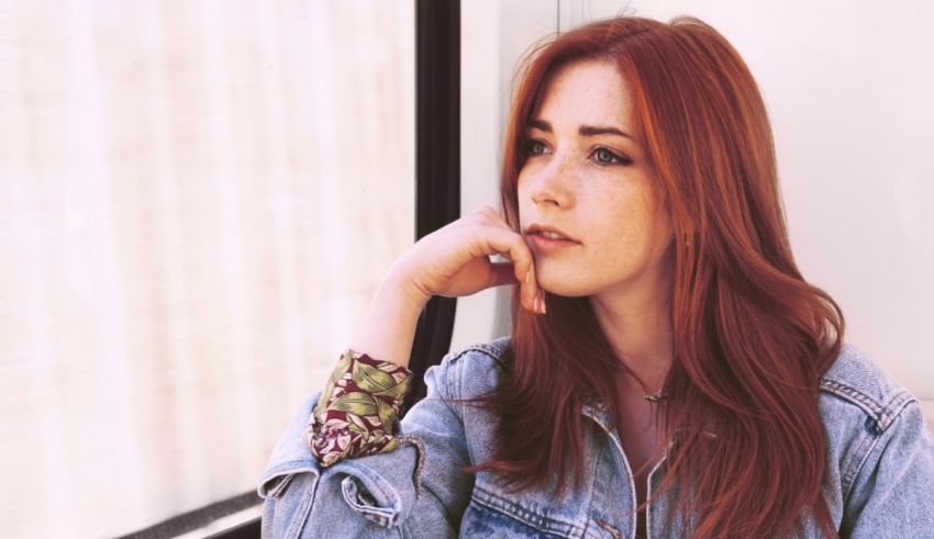 A woman with red hair is sitting in front of a window.