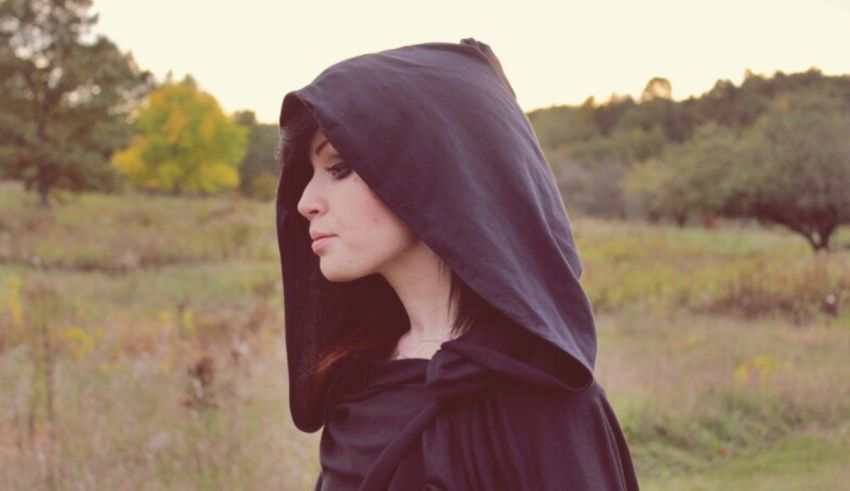 A woman wearing a black hooded coat in a field.