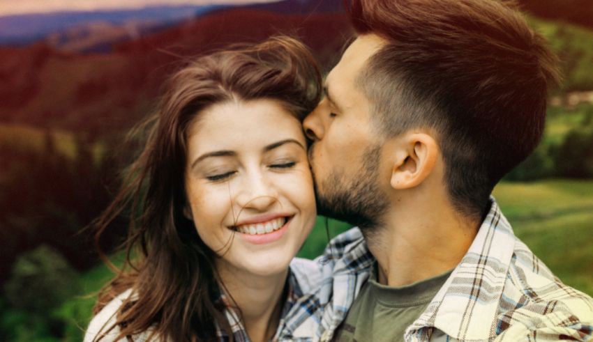 A man and woman kissing in front of a mountain.