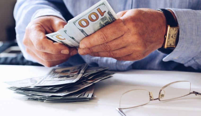 A man is holding a stack of money on a desk.