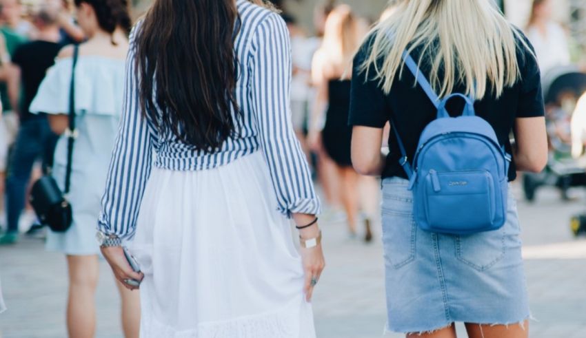 Two women walking down the street with a blue backpack.