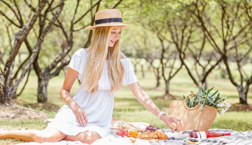 A woman in a white dress is sitting on the grass with a picnic basket.