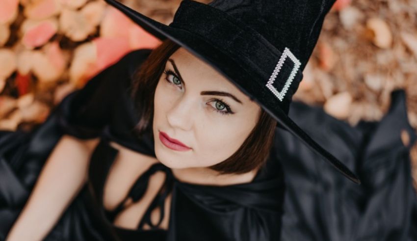 A woman in a black witch hat laying on leaves.