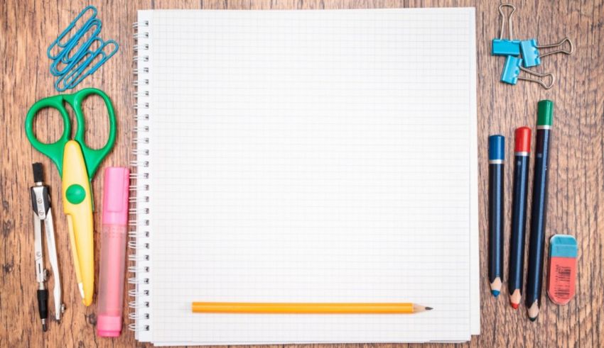 A notebook, pencils and other school supplies on a wooden table.