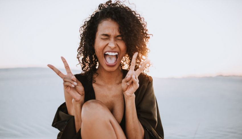 A woman with curly hair making a peace sign in the sand.