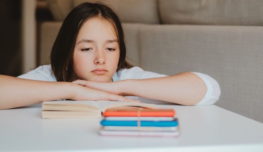 A girl is sitting at a table with a book in front of her.