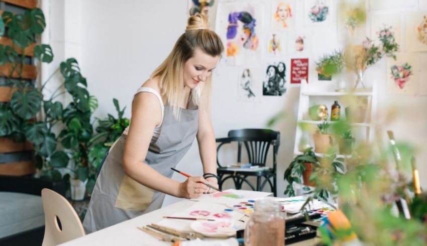 A woman in an apron is painting in her art studio.