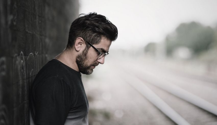 A man leaning against a wall next to a train track.
