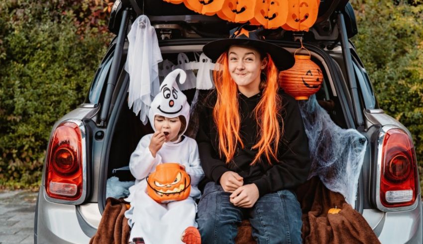 A woman and child sitting in the trunk of a car with halloween decorations.