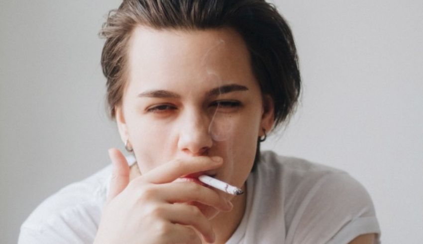 A woman smoking a cigarette in front of a white background.