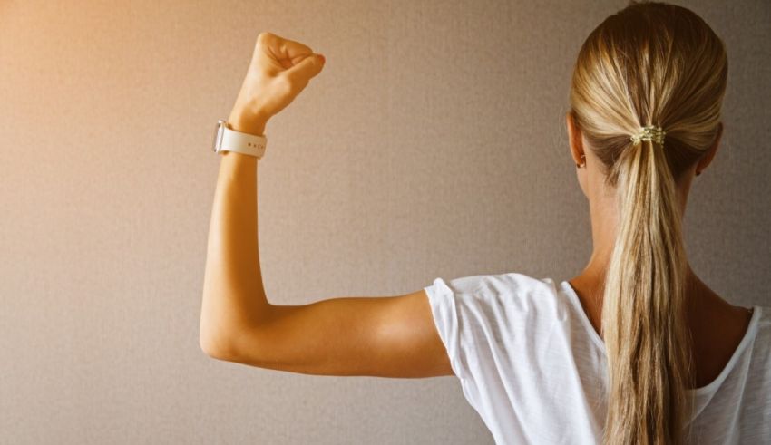 A woman is flexing her biceps in front of a wall.