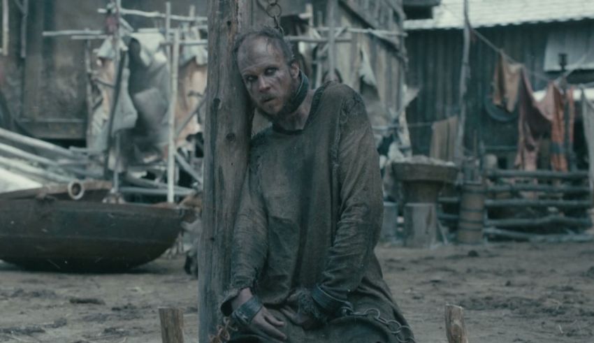 A man sitting on a wooden bench in a dirty area.