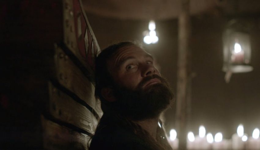 A bearded man in a dark room with candles.