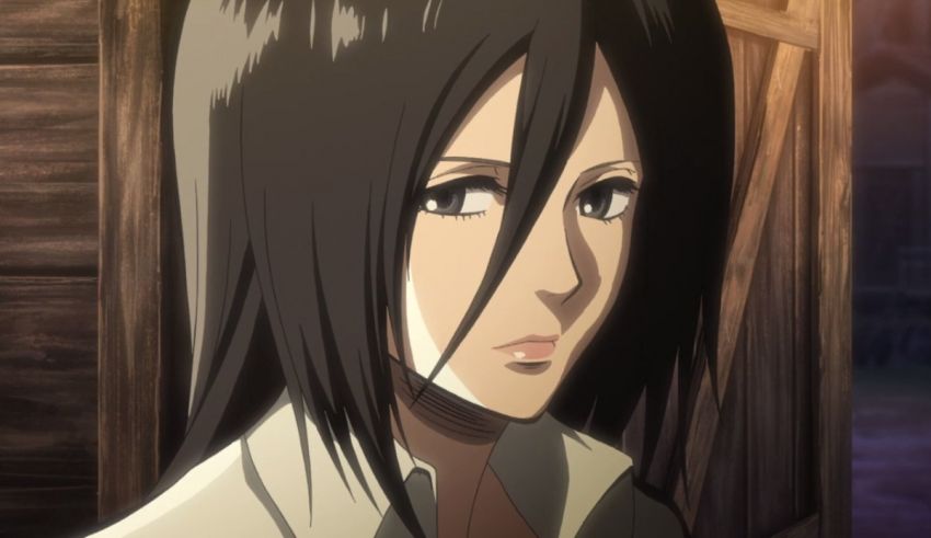 A woman with long black hair standing in front of a wooden door.