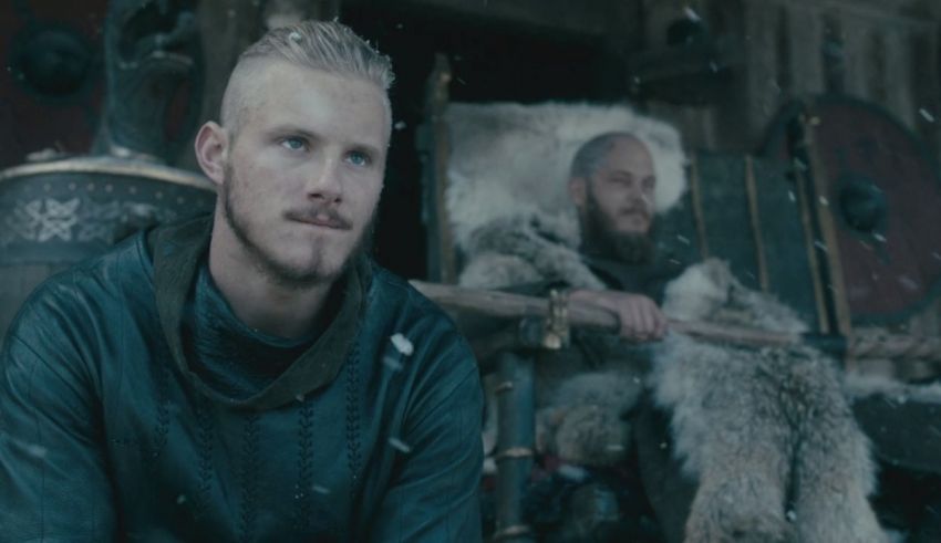 A man in a viking costume is sitting in front of a snowy cabin.