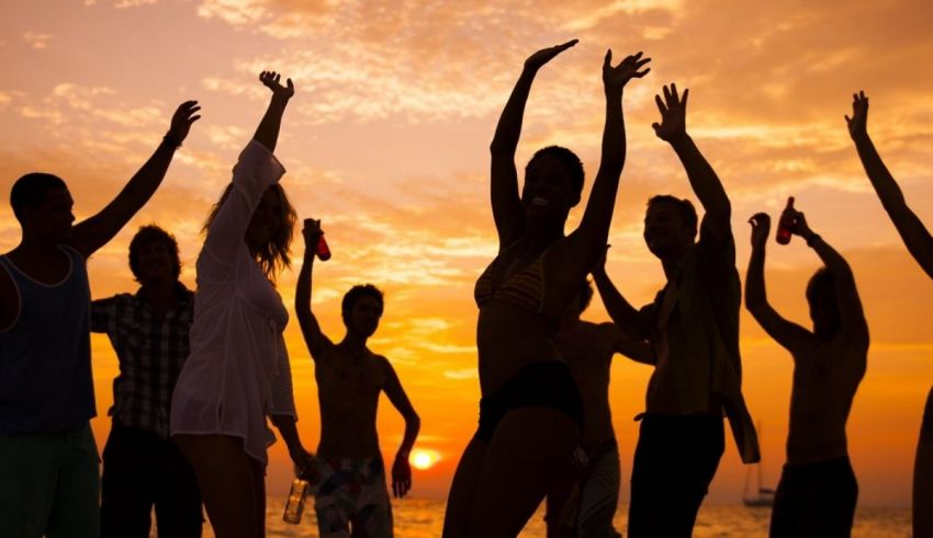 A group of people dancing on the beach at sunset.