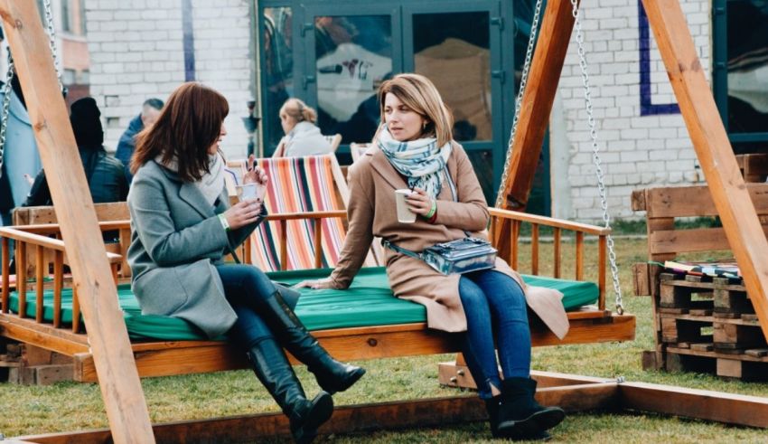 Two women sitting on a swing at an outdoor event.