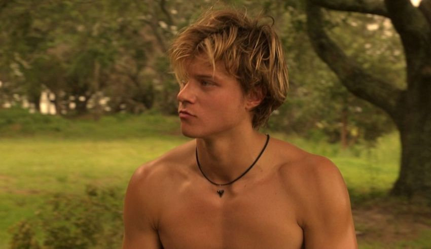 A shirtless man sitting in a grassy area.