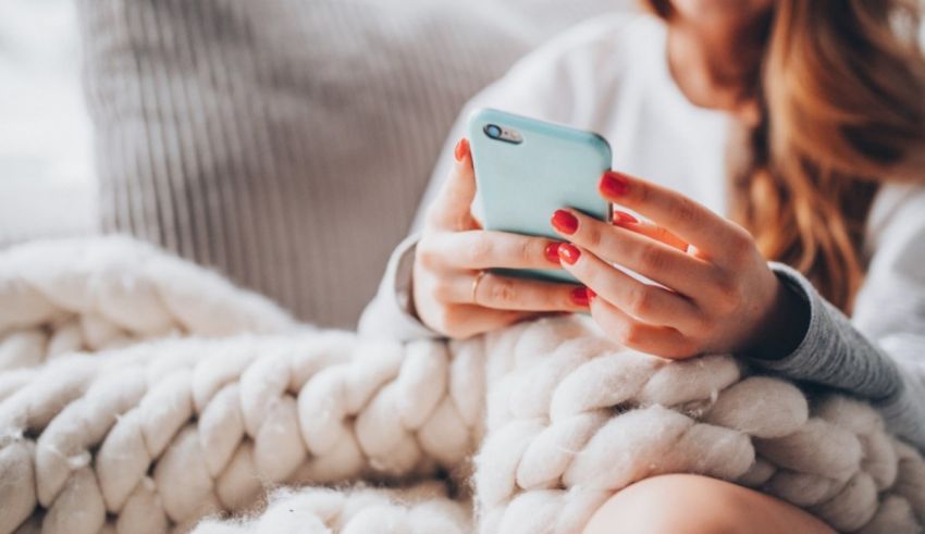 A woman holding a cell phone while sitting on a blanket.