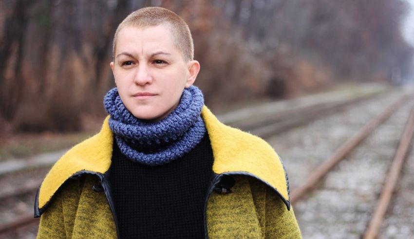 A woman in a yellow jacket standing next to train tracks.