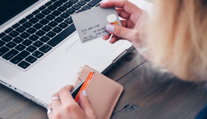 A woman is holding a credit card in front of a laptop.