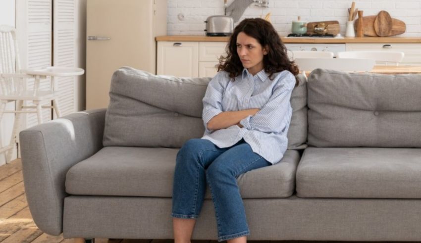 A woman sitting on a gray couch in a kitchen.