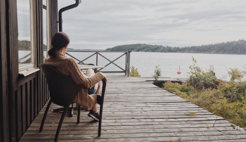 A woman sitting in a chair on a deck overlooking a lake.