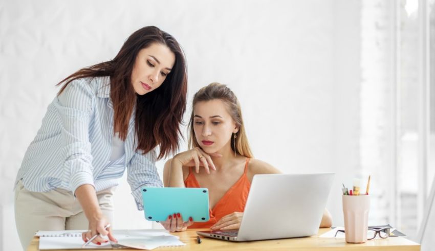 Two women sitting at a desk and looking at a laptop.