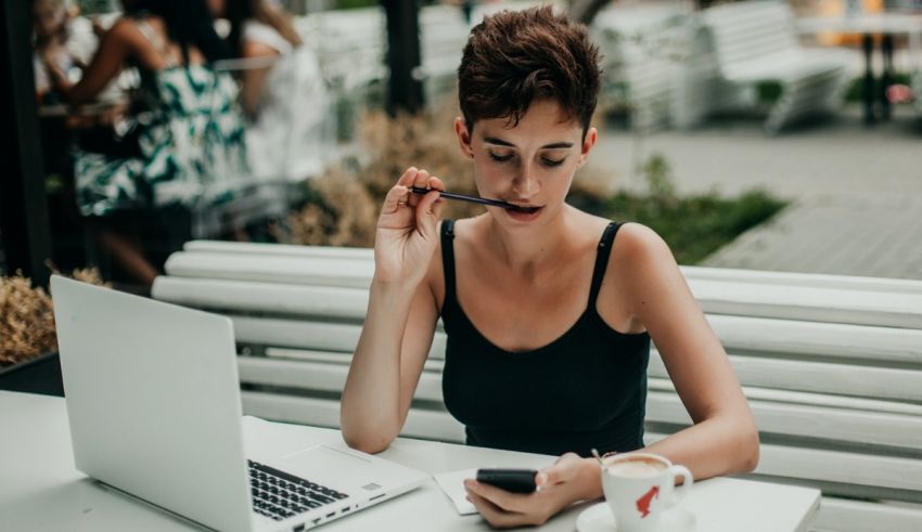 A woman sitting at a table with a laptop and cell phone.