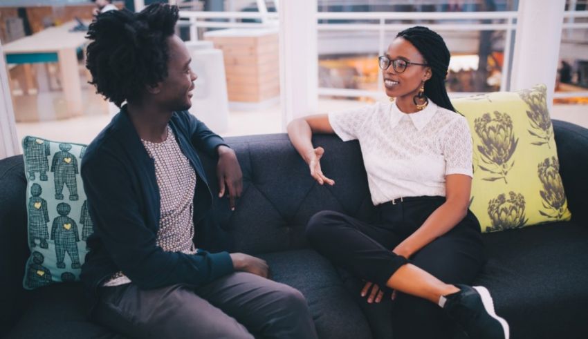 Two people sitting on a couch talking to each other.