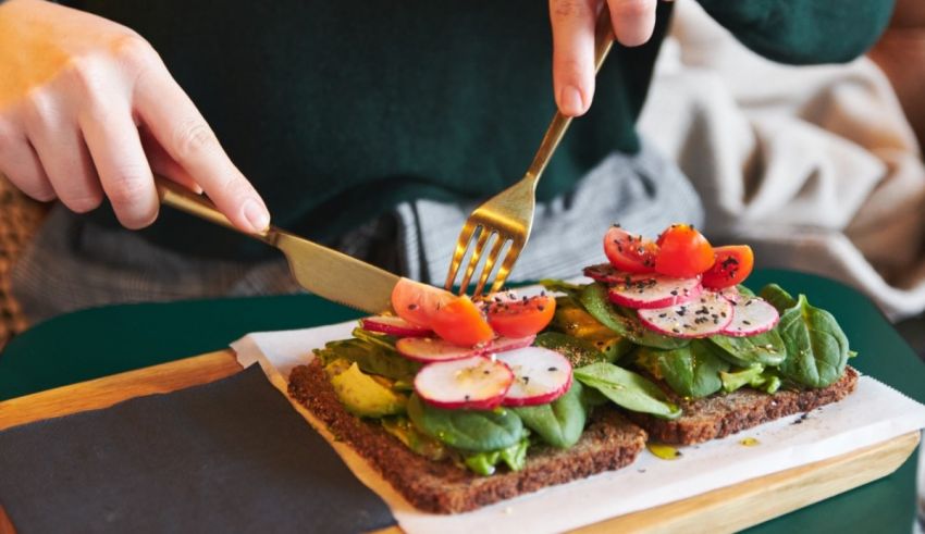 A woman is cutting a sandwich with a fork.