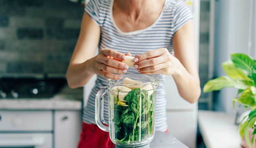 A woman is blending spinach in a blender.