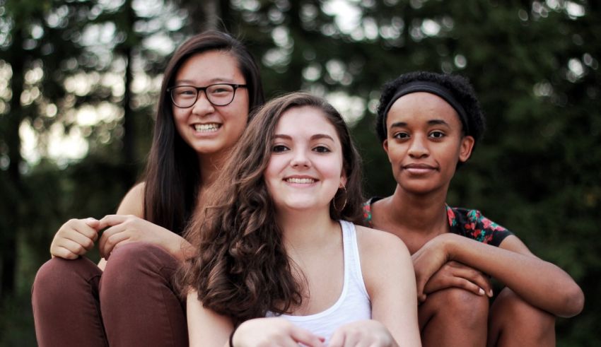 Three young women sitting on the ground in front of a tree.