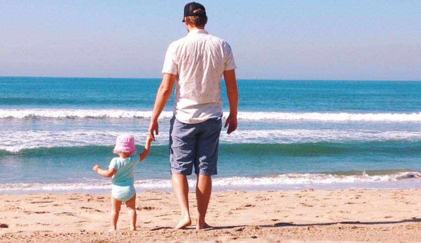 A man and a little girl walking on the beach.