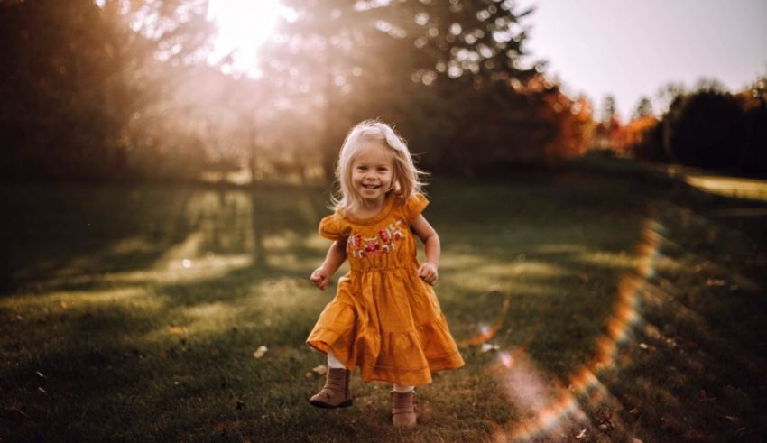 A little girl in a yellow dress running in the grass.