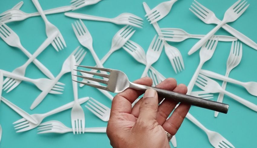 A person holding a fork in front of a bunch of plastic forks.
