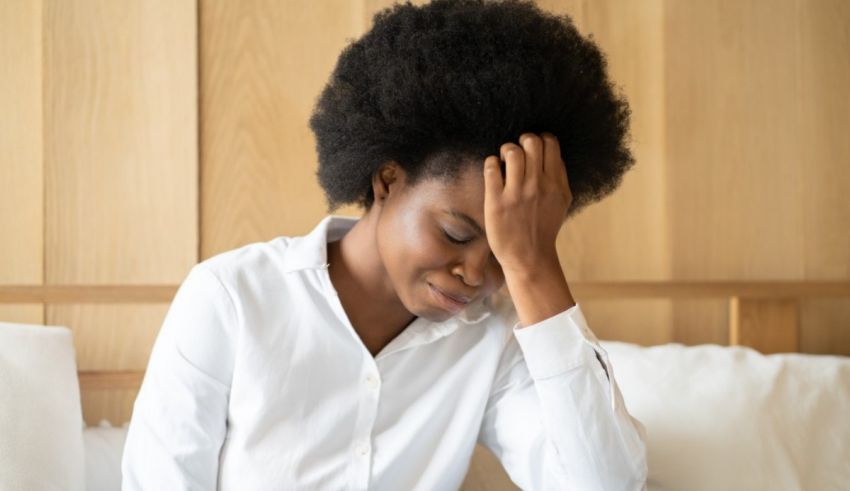 A woman with afro hair is sitting on a bed with her head on her head.