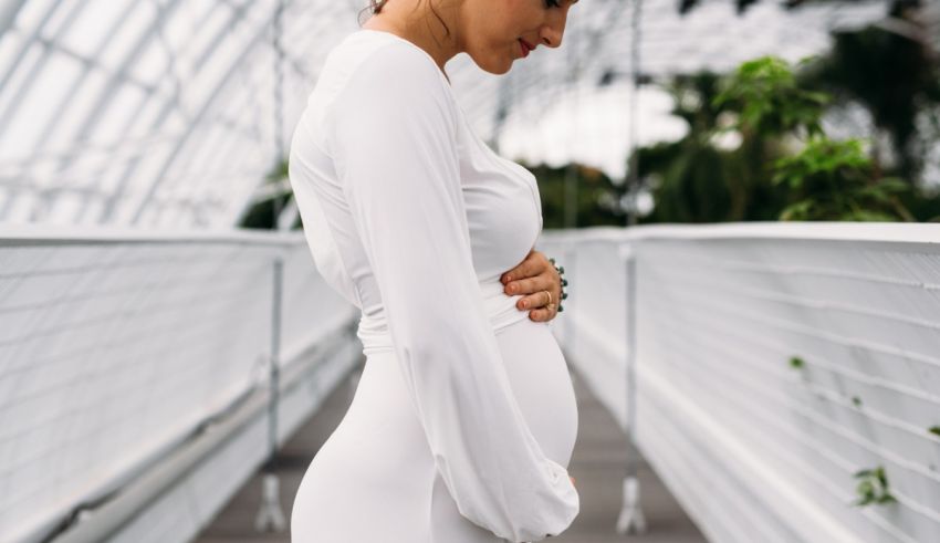 A pregnant woman in a white dress standing in a greenhouse.
