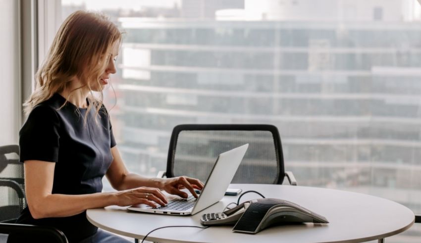 A woman sitting at a desk with a laptop in front of a window.