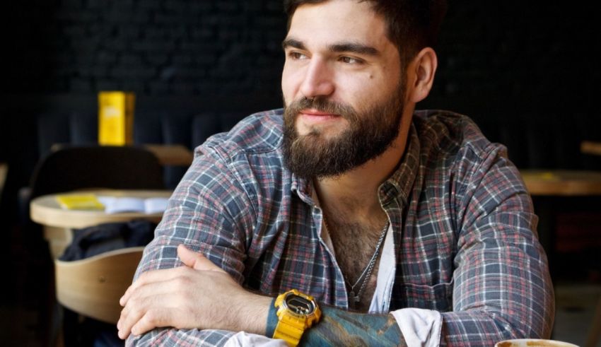 A bearded man sitting at a table with a cup of coffee.