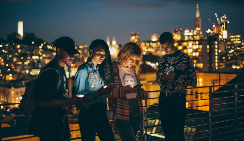 A group of young people looking at their cell phones at night.